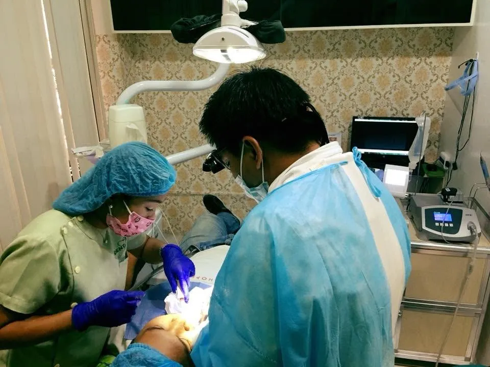 Dr. Eden Anthony Reyes, gowned and masked, performing oral surgery with a dental assistant at iDent Dental Lounge in Cagayan de Oro
